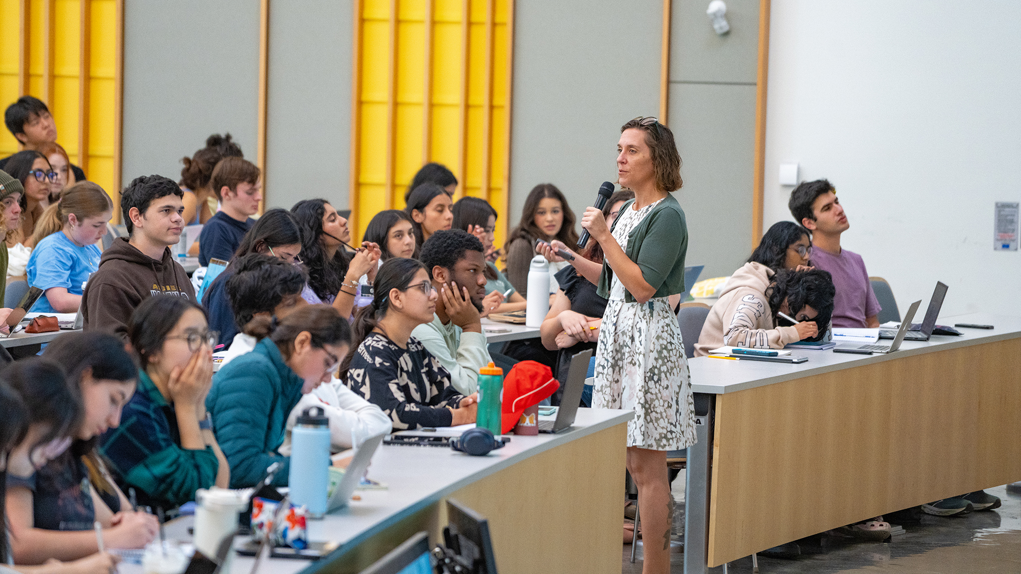 Instructor speaking into microphone while teaching biology lecture to students in large classroom