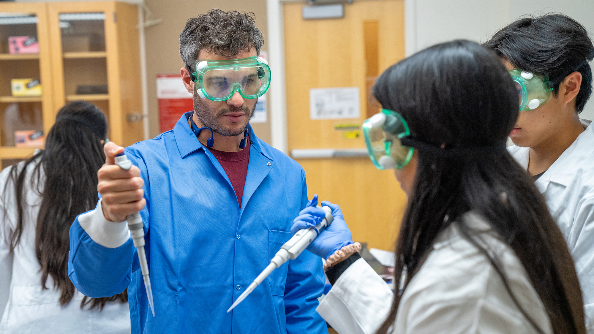 Instructor and students wearing goggles using pipettes during a biology lab training session