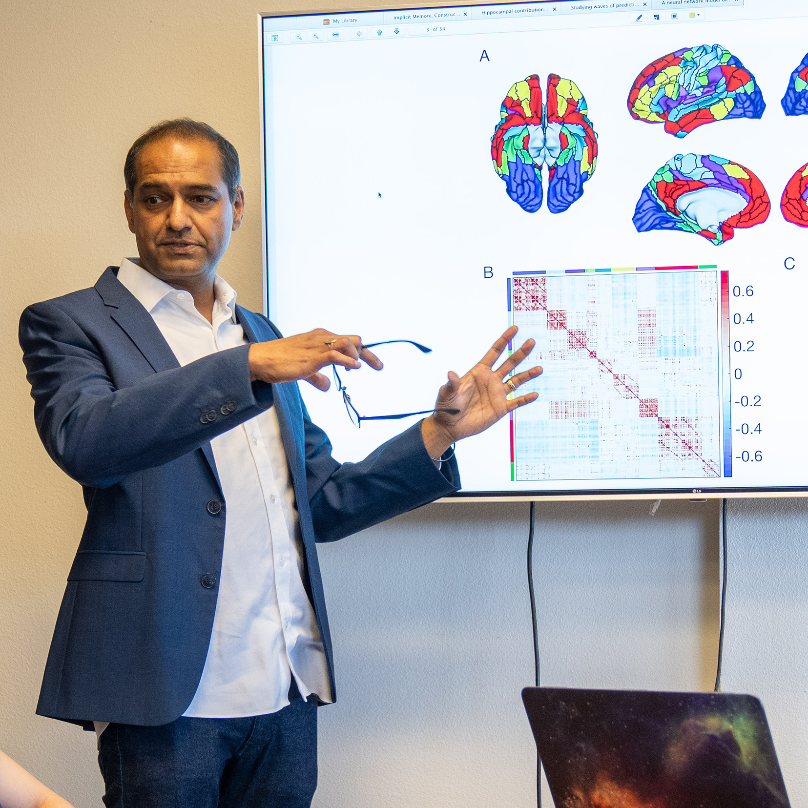 Male researcher standing in front of presentation display screen showing colorful renderings of the brain.