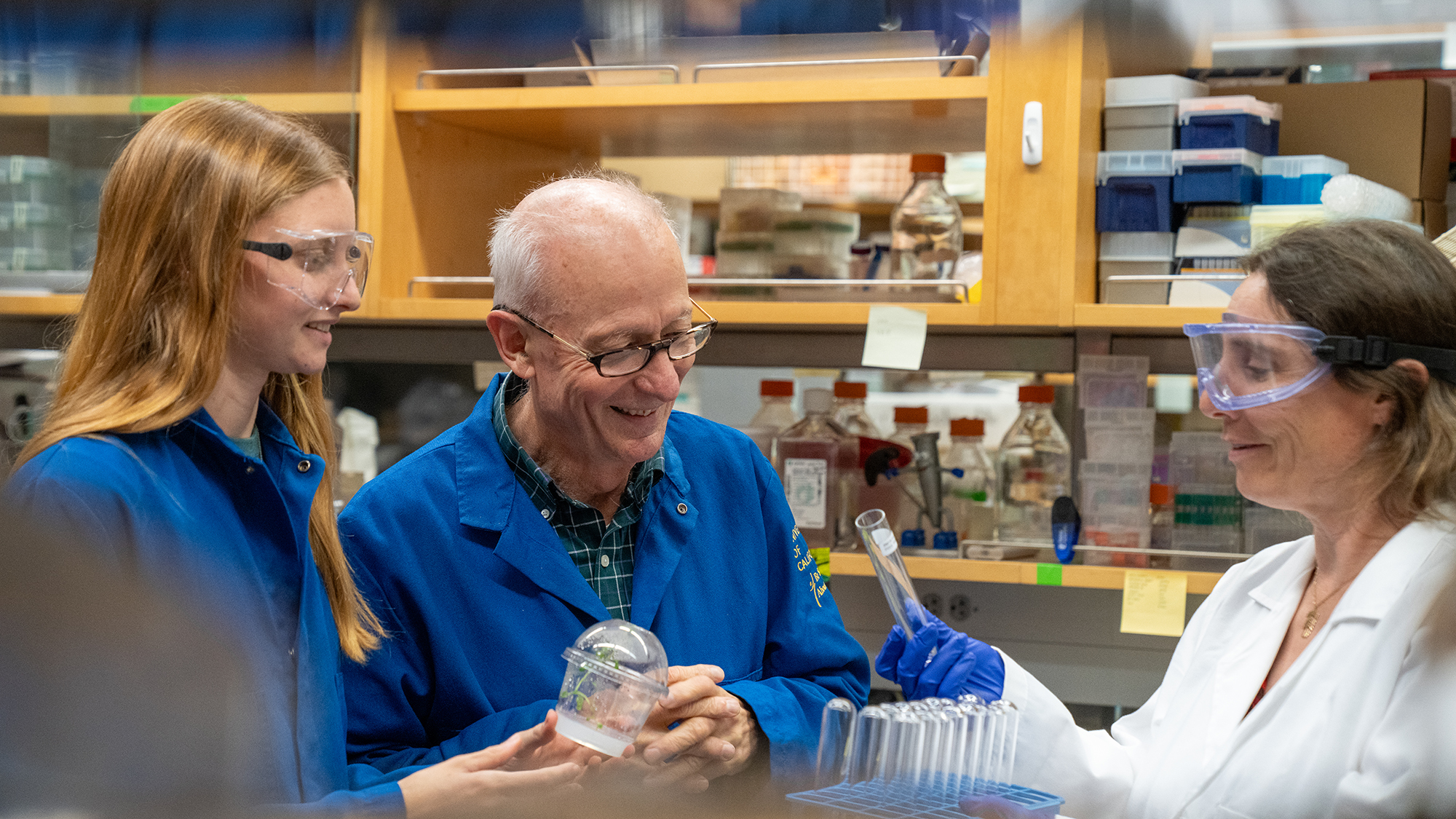 Three people in a laboratory setting examining a test tube with lab supplies in the background.