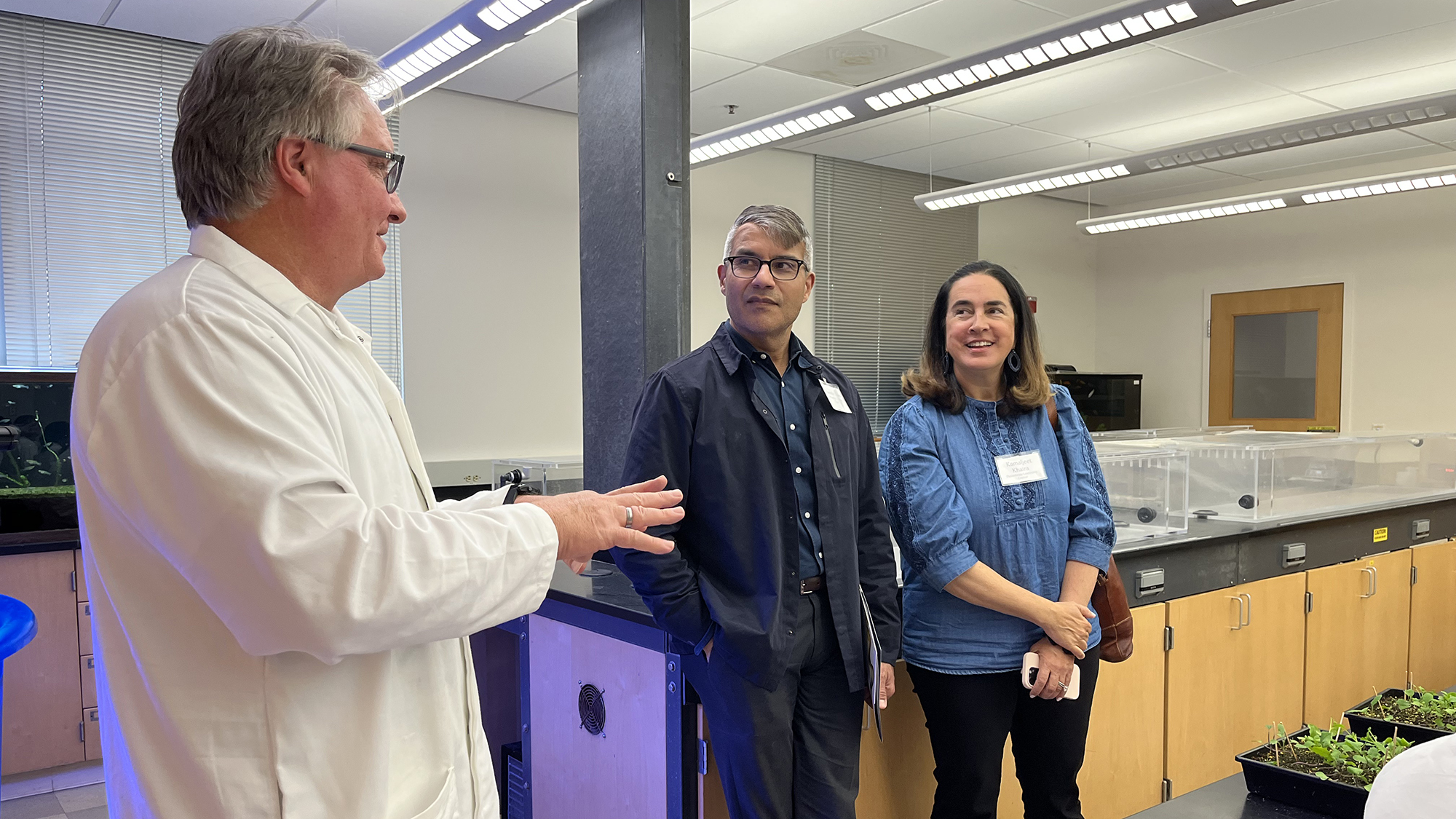 Three people in a science lab: man in white coat talks to two smiling students