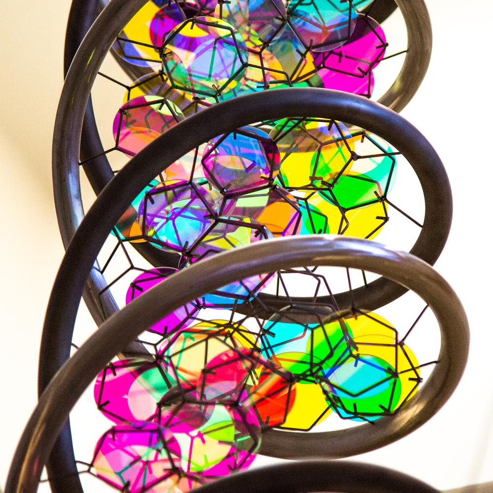Close-up of a colorful, abstract double helix sculpture with geometric facets and iridescent reflections inside spiral metal loops.