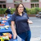 A friendly UC Davis staff member wearing a UC Davis polo shirt engages in conversation with two students at an outdoor information fair. Tables covered with snacks are visible in the background.