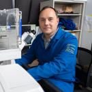 Researcher in a UC lab coat sits beside advanced microscope equipment, preparing for imaging work in the laboratory.