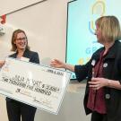 Two women standing in front of a presentation screen and holding an oversized check